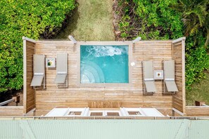 An outdoor hot tub with two lounge chairs and a small table, surrounded by wooden decking and lush greenery.