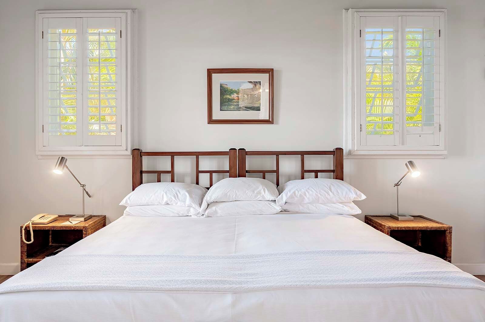 A neatly made bed with white linens, two bedside lamps, and a framed picture on the wall.