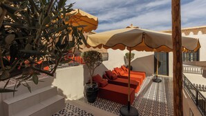 A terrace with a patterned floor, orange seating, and a large umbrella. - Riad Cedrat (Marrakech)