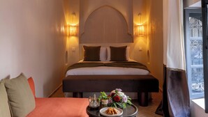 A hotel room with a bed, a sofa, a small table with a flower arrangement, and a window with curtains. - Riad Cedrat (Marrakech)