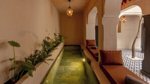 A corridor with a water feature, seating area, and hanging lights. - Riad Cedrat (Marrakech)