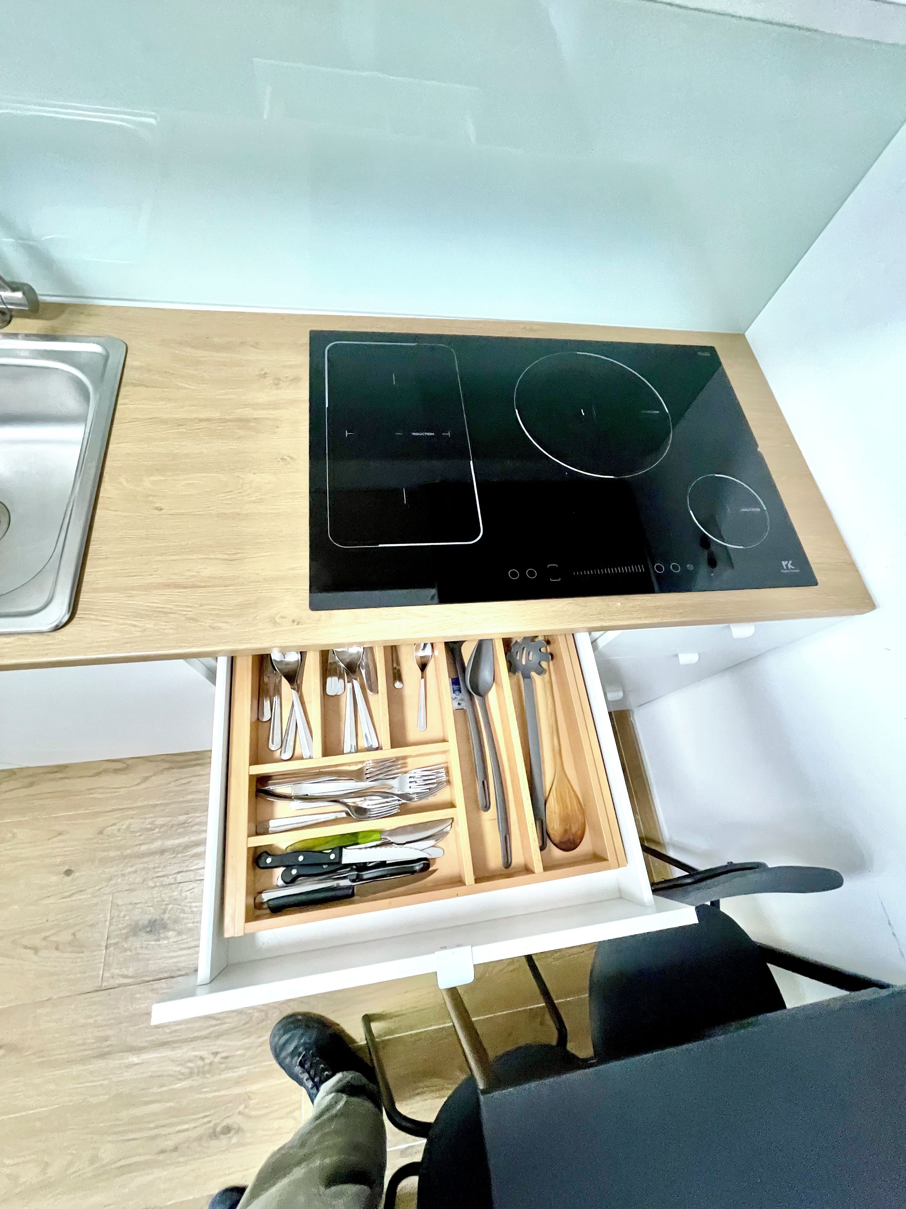 A kitchen with a built-in induction cooktop, a wooden countertop, and a drawer with various utensils.
