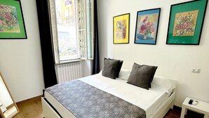 Ein Schlafzimmer mit einem Bett, einem Fenster mit Vorhängen und drei gerahmten Bildern an der Wand.