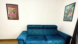Ein Zimmer mit einem blauen Sofa, Holzböden und zwei gerahmten Kunstwerken an den Wänden.