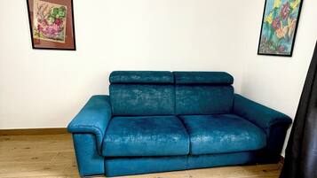 Ein Zimmer mit einem blauen Sofa, Holzböden und zwei gerahmten Kunstwerken an den Wänden.