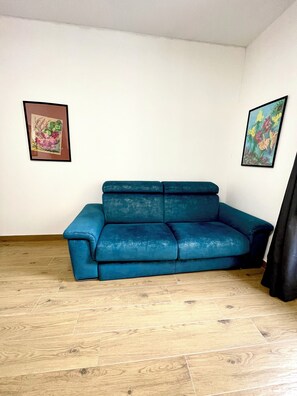 A room with a blue sofa, wooden flooring, and two framed artworks on the walls. - CameliaHouse Modern two-room apartment -45 m² 4 beds (Roma)