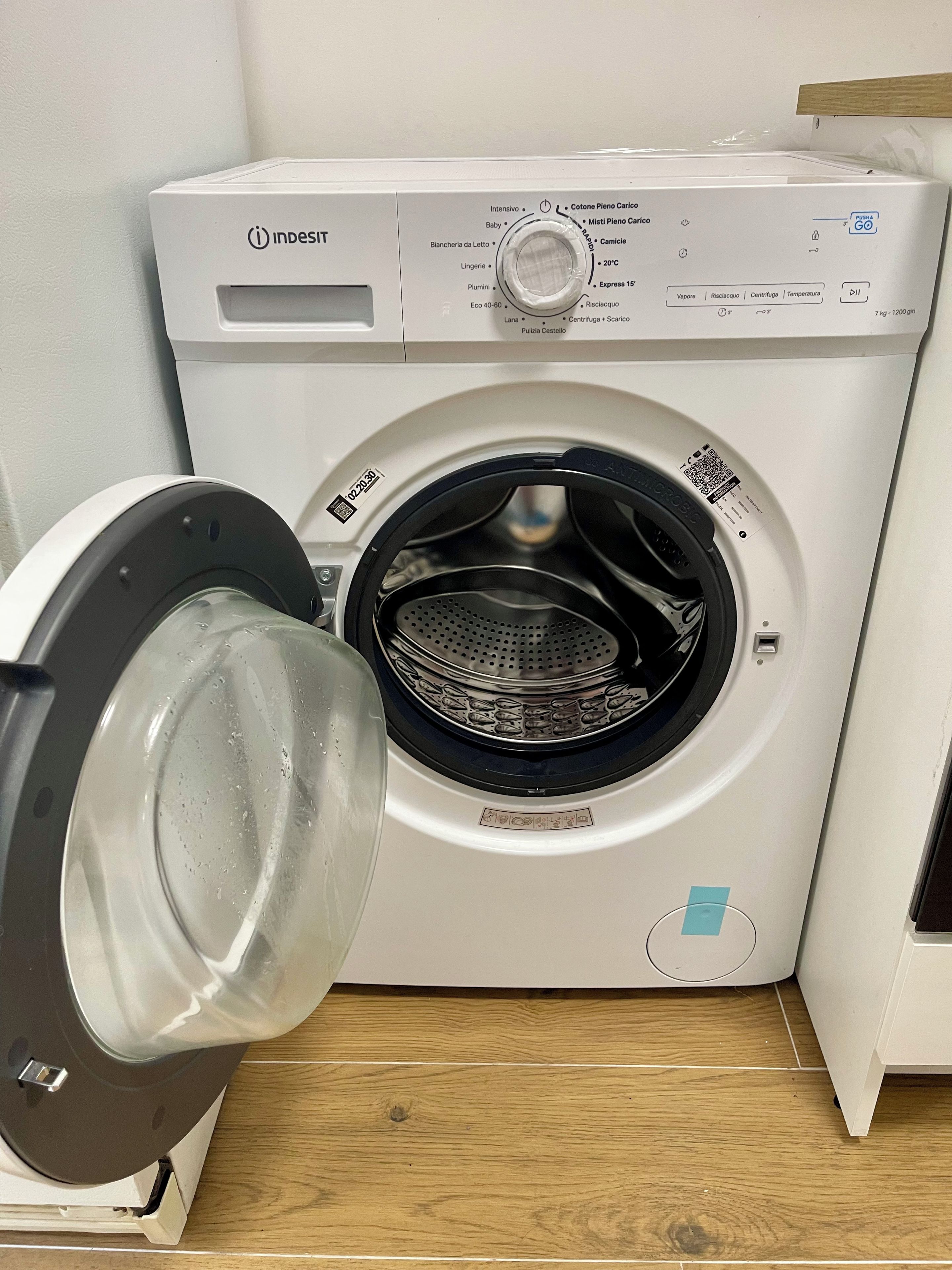 Eine Waschmaschine mit Frontlader, einer Bedienkonsole, einem Wasseranschluss und einem Ablauf.