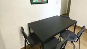 Ein Essbereich mit einem schwarzen Tisch und vier Stühlen, ein gerahmtes Blumenbild an der Wand und eine Klimaanlage im Hintergrund.