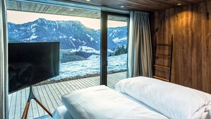 Une chambre avec un lit, une télévision, une échelle en bois et une vue sur des montagnes enneigées.