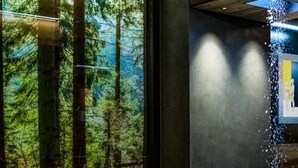 Un intérieur moderne avec une grande fenêtre donnant sur une forêt, un mur éclairé de lumière bleue et un sol carrelé.