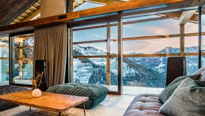 Un salon moderne doté d’une grande fenêtre donnant sur les montagnes, d’une table basse en bois, d’un canapé vert et d’un vase décoratif.