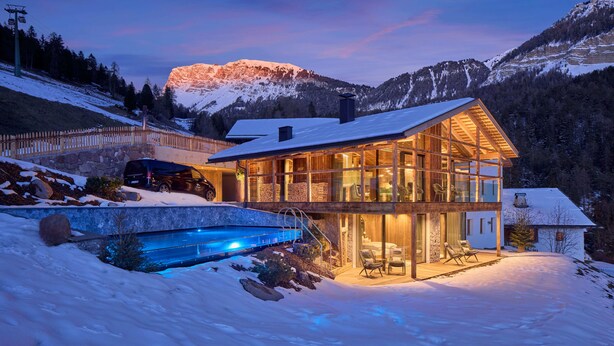 Une maison moderne avec une façade en verre, une piscine et une vue sur des montagnes enneigées.