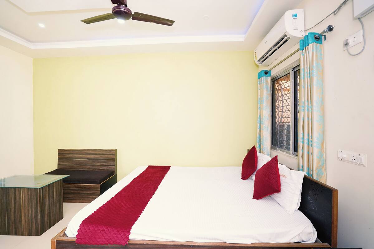 A bedroom with a bed, a bedside table, a chair, a ceiling fan, and an air conditioning unit.