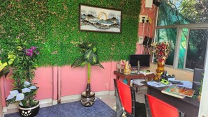 A room with a desk, chairs, a computer, and a wall decorated with greenery and a framed picture. - PURNI HOTEL  (Kanthi)