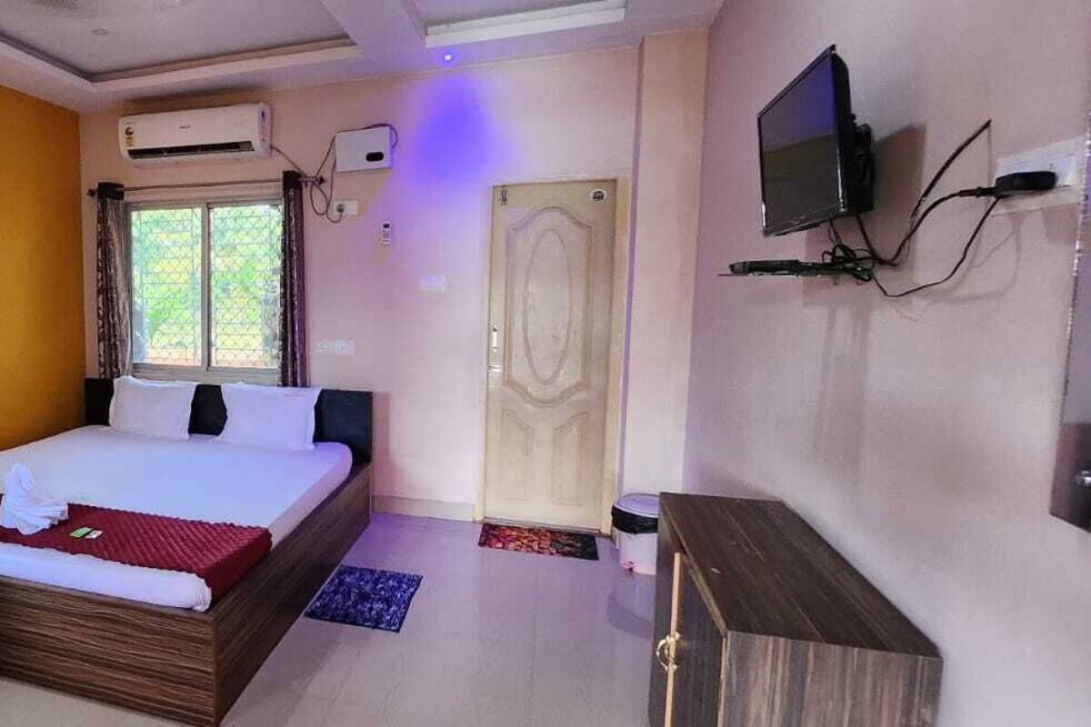A hotel room with a bed, a TV, an air conditioning unit, and a window with curtains.
