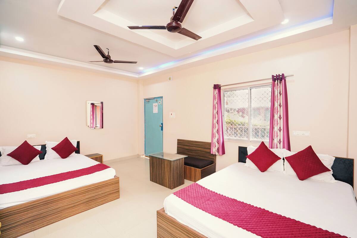 A hotel room with two beds, a ceiling fan, a small table, and a window with curtains.