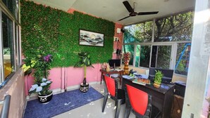 A room with a desk, two chairs, a ceiling fan, a TV, and a wall decorated with green foliage and a framed picture. - PURNI HOTEL  (Kanthi)