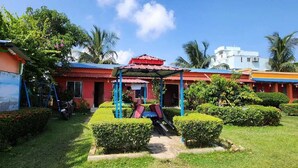 A courtyard with a gazebo, neatly trimmed bushes, and a mural on the building. - PURNI HOTEL  (Kanthi)