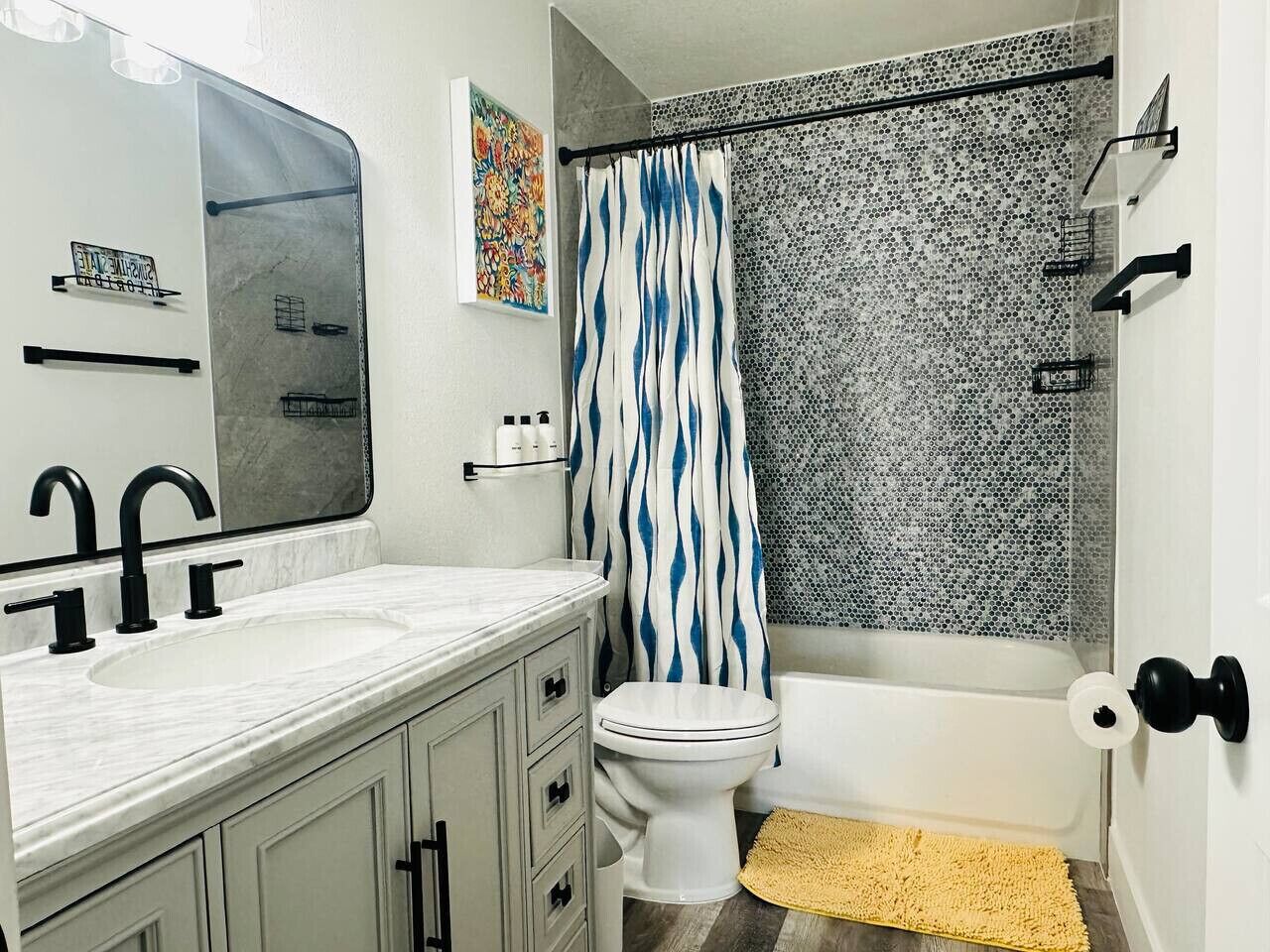 A bathroom with a white sink, black faucets, a white toilet, a shower with a blue and white striped curtain, and a mosaic shower wall.