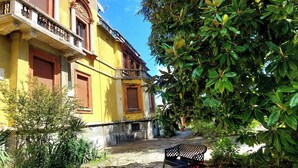 A courtyard with a stone pathway, a bench, and a yellow building with ornate balconies.