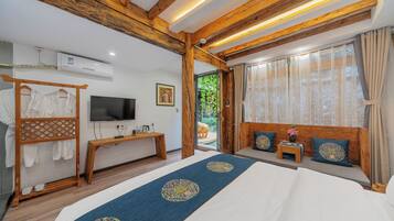 A hotel room with a wooden ceiling, a bed with a blue runner, a TV, a bench, and a window with curtains.