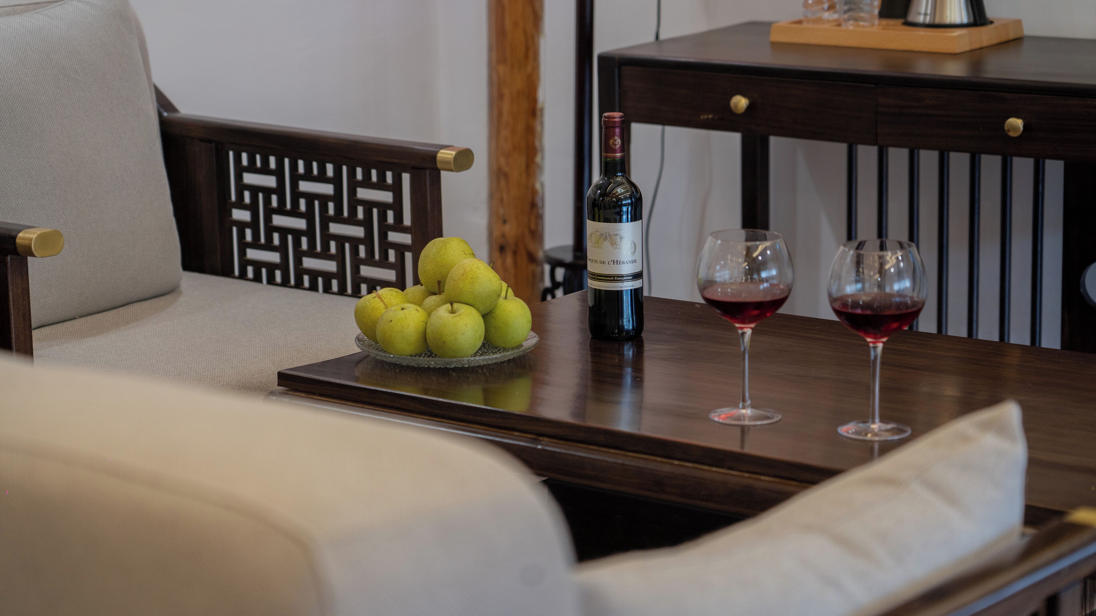 A dining table with a bottle of wine, two wine glasses, and a bowl of pears.