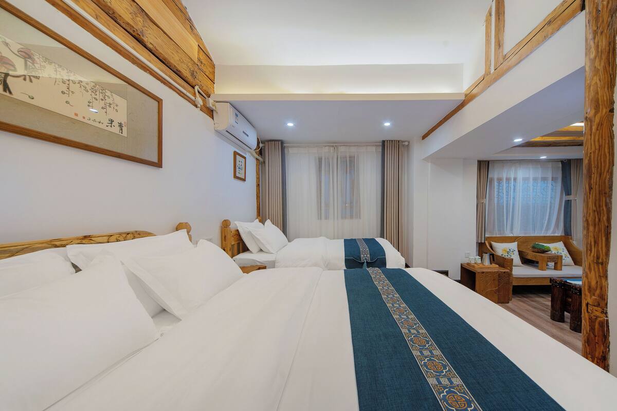 Une chambre d’hôtel avec deux lits, des têtes de lit en bois, une grande œuvre d’art encadrée, un climatiseur et une petite table en bois avec une chaise.