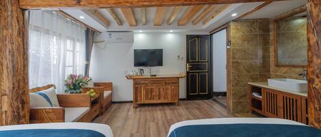 A room with two beds, wooden beams on the ceiling, a TV, a wooden cabinet, a sink, and a window with curtains.