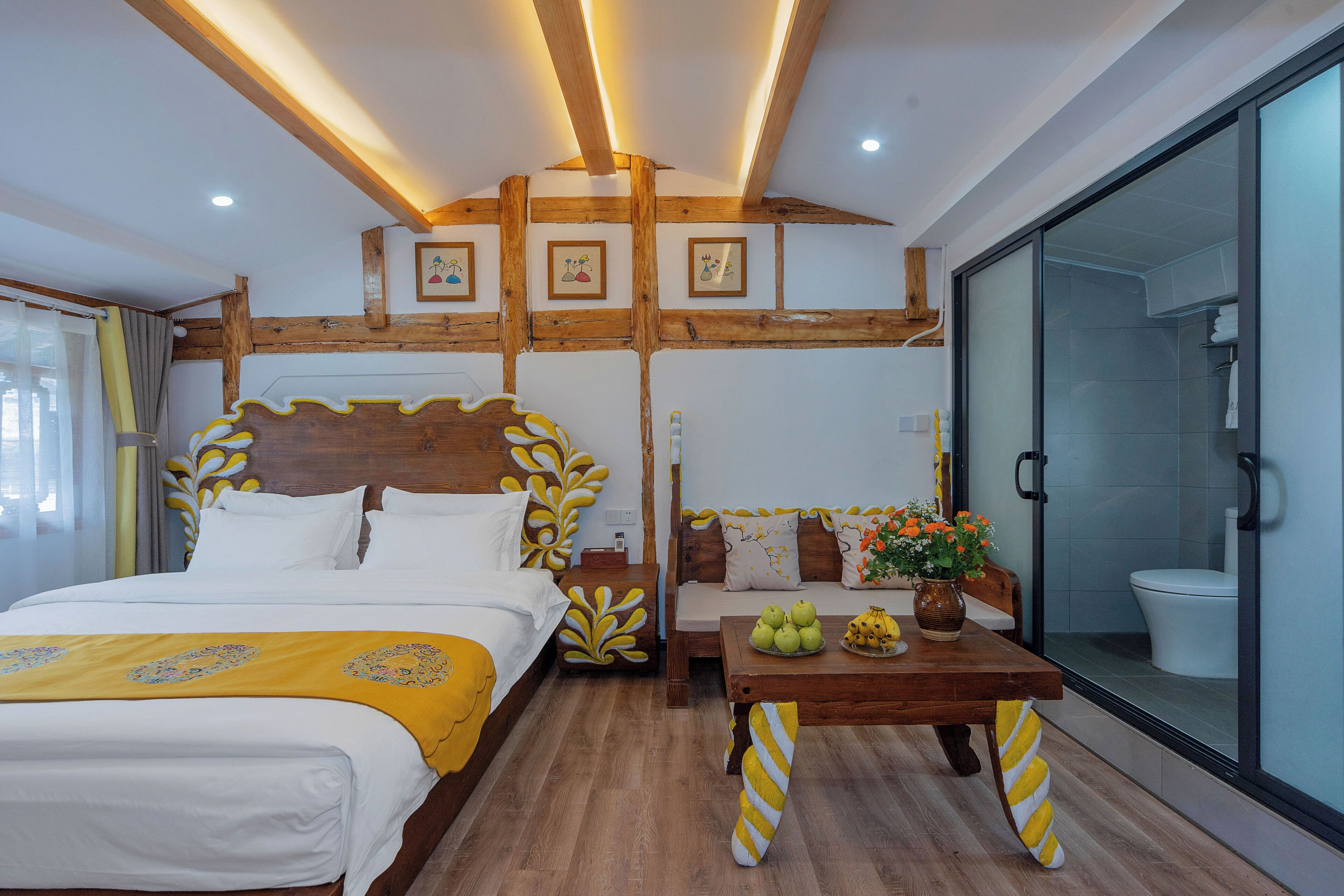 A hotel room with a large bed, a wooden headboard, a sofa, a small table with fruit, and a glass shower enclosure.