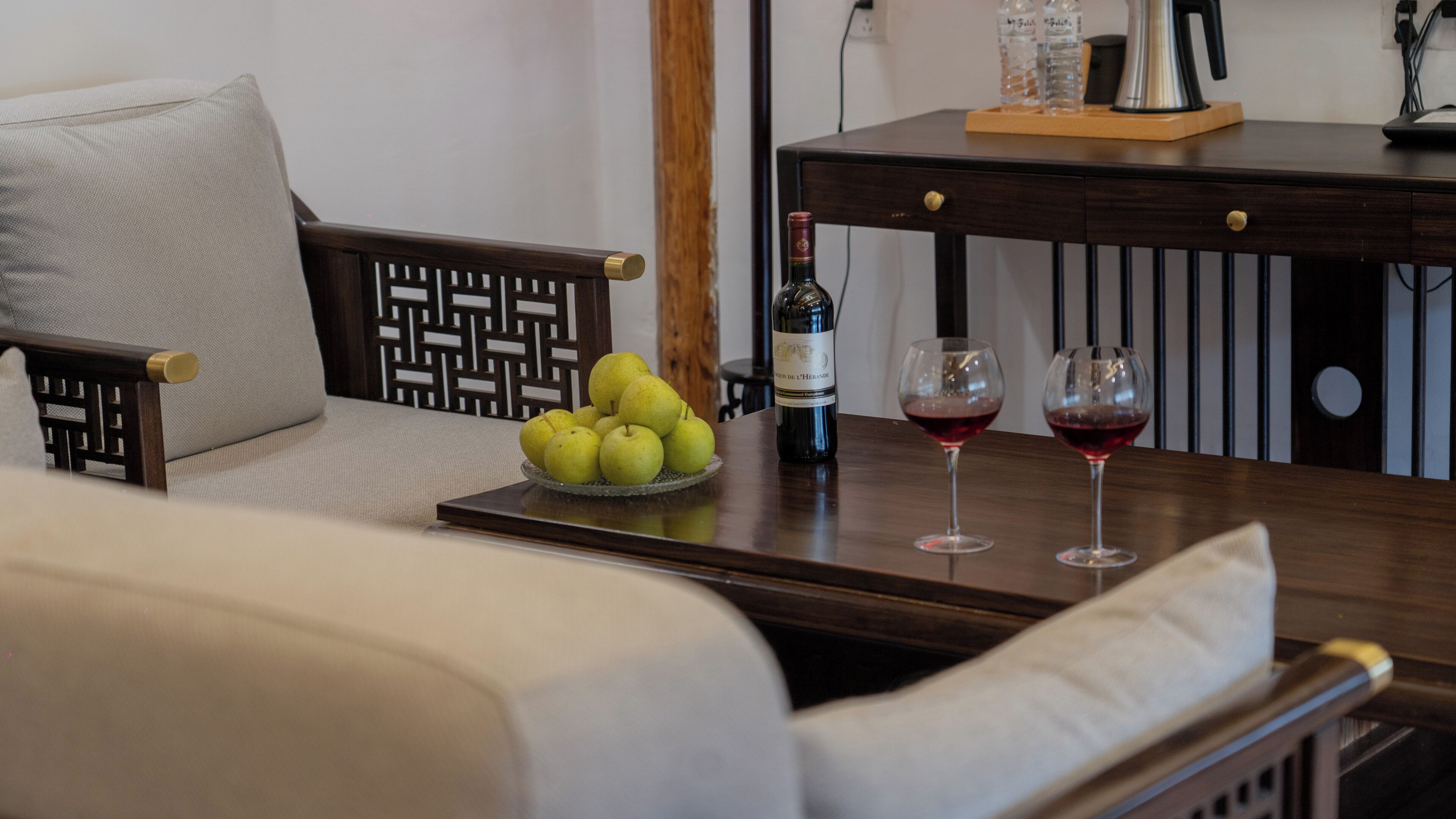 A wooden table with a bottle of wine, two wine glasses, and a bowl of pears.