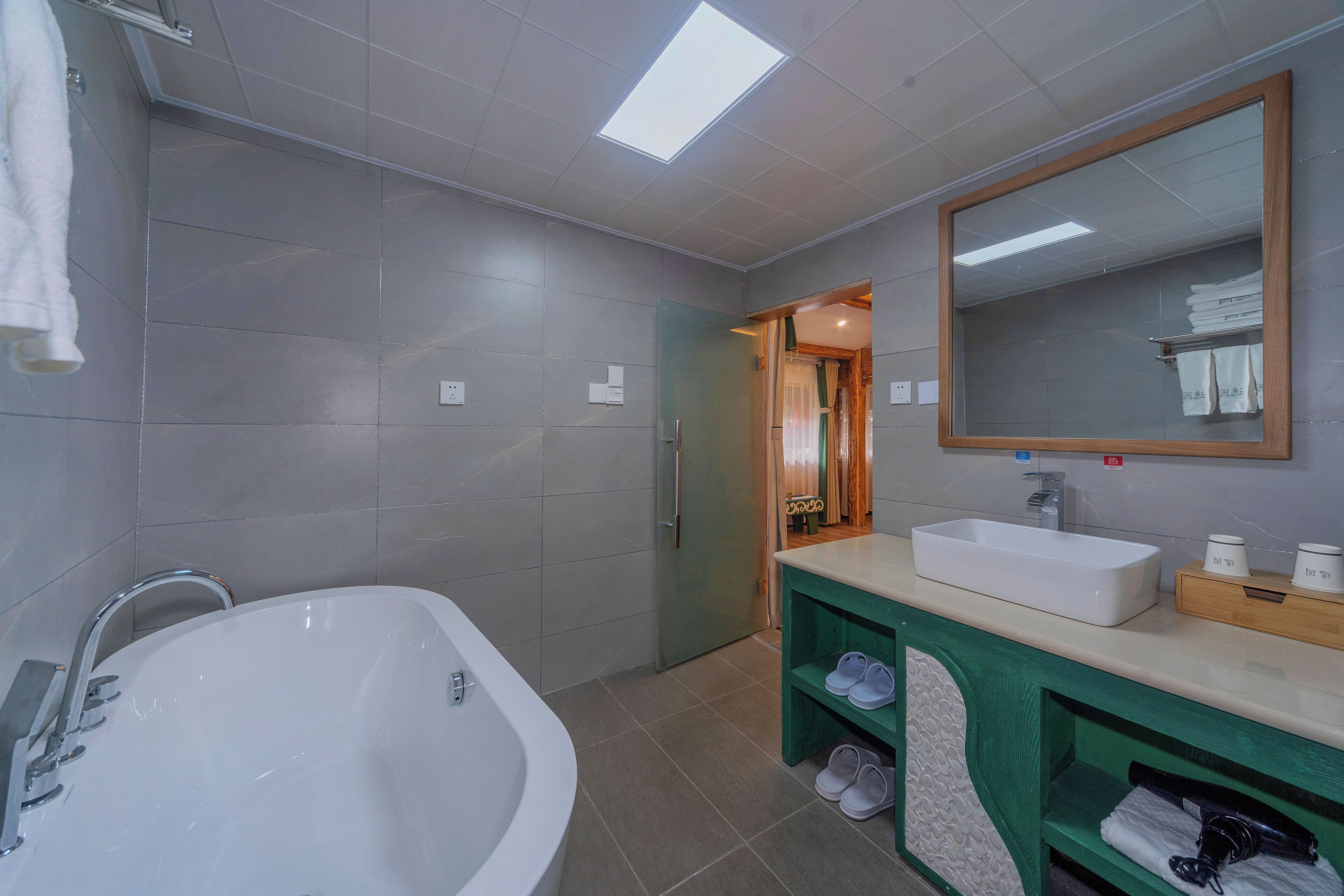 Un baño moderno con una bañera independiente, un espejo grande y un tocador con lavabo y toallero.