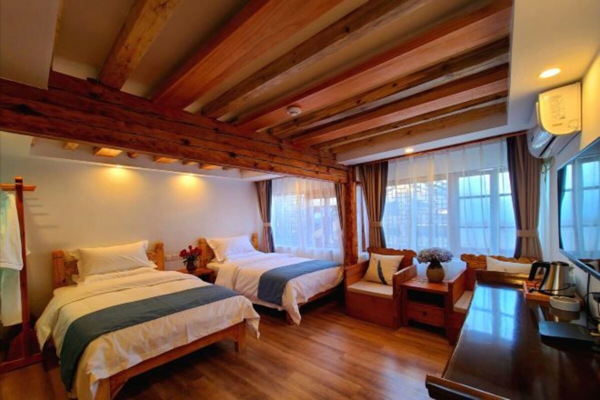 Een kamer met twee bedden, houten balken in het plafond, een kleine tafel met een lamp en een raam met gordijnen.