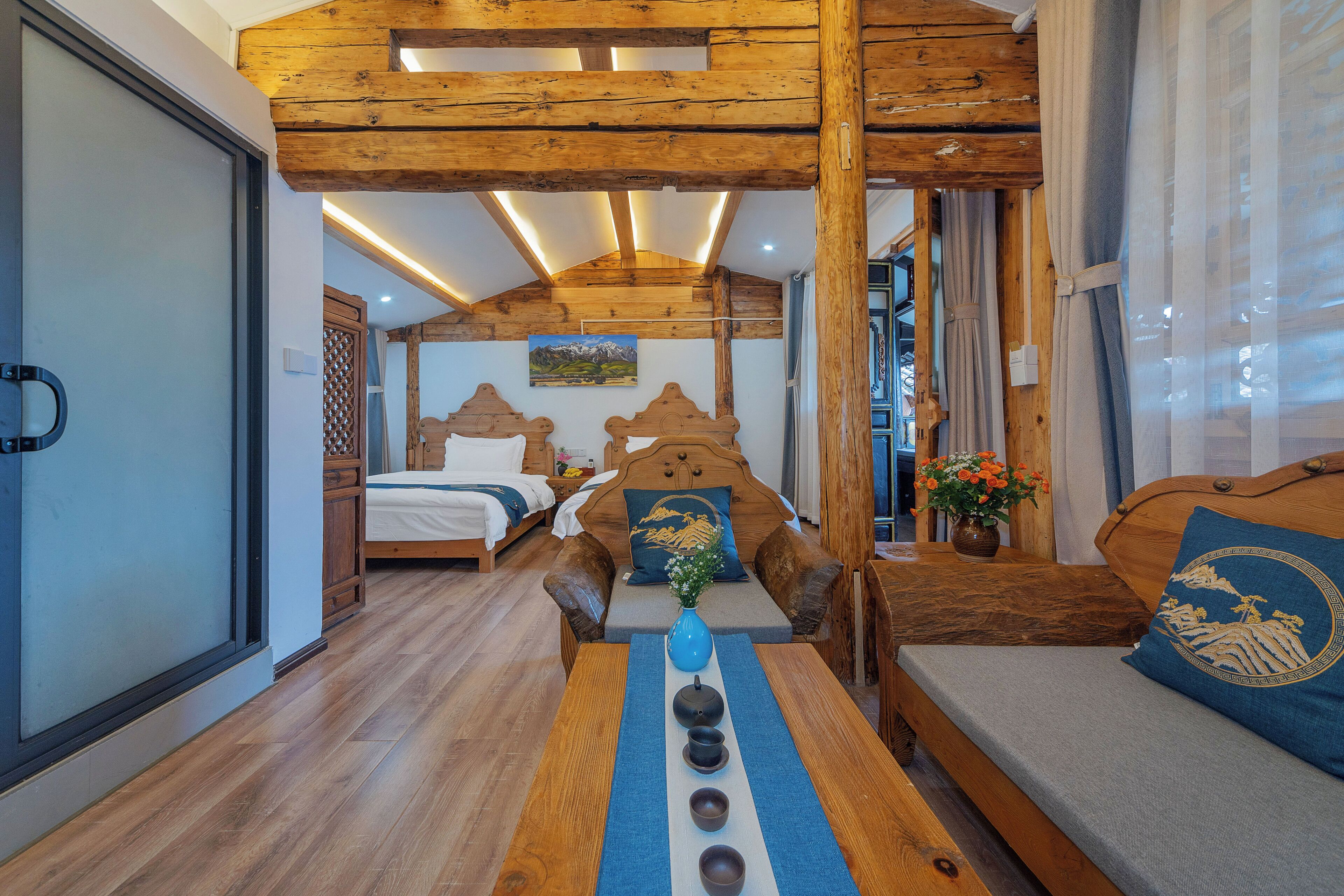 Una camera accogliente con soffitto in legno, un letto con cuscino a tema montagna, un divano con un cuscino e un tavolo con un vaso e tazze.