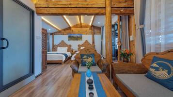 A cozy room with a wooden ceiling, a bed with a mountain-themed pillow, a sofa with a cushion, and a table with a vase and cups.