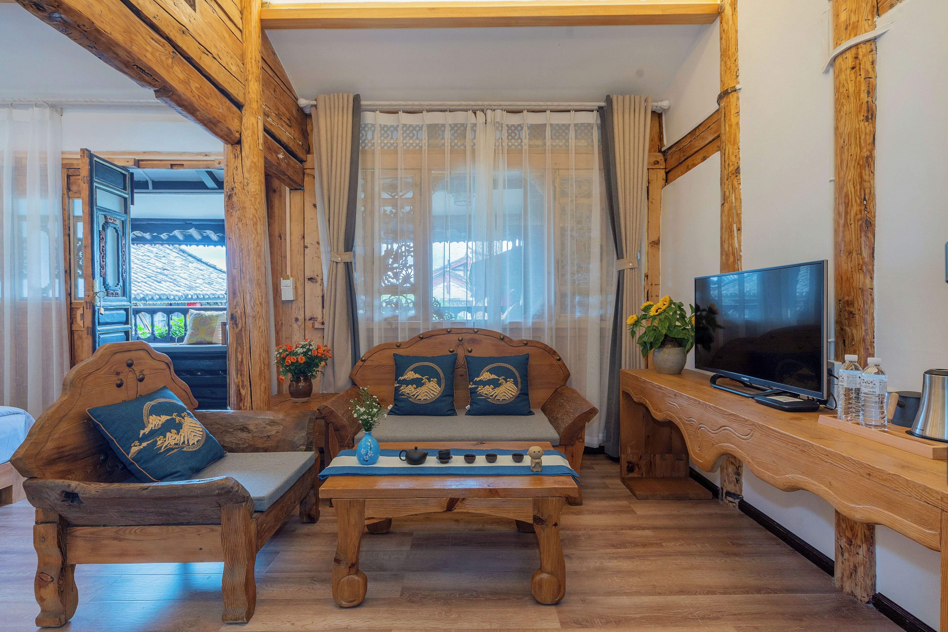 A traditional wooden sofa with cushions, a small table with a vase and teapot, and a television on a wooden stand.