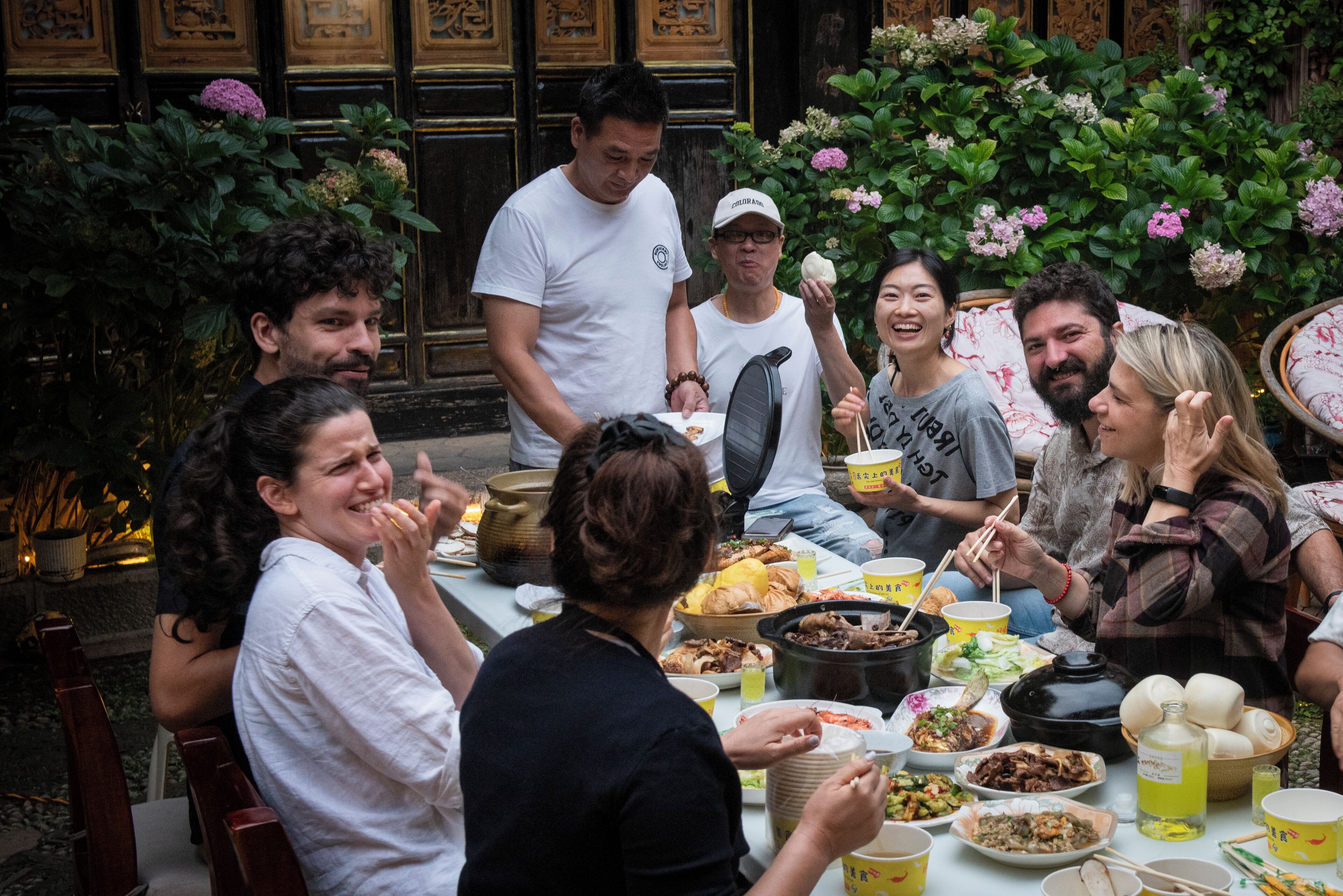 A group of people dining outdoors at a table with various dishes and drinks.