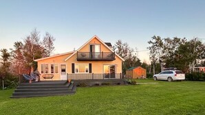 A two-story house with a balcony, a front porch, and a small attached garage. - Ocean View Cottage, With Access To Tracadie Bay-Minutes From Blooming Point (Mount Stewart)
