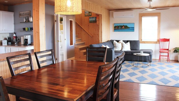 A wooden interior with a dining table, chairs, a sofa, and a red chair. - Ocean View Cottage, With Access To Tracadie Bay-Minutes From Blooming Point (Mount Stewart)