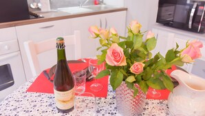 A dining table with a bottle of wine, a vase of roses, and a pitcher. - Gîte De La Voûte in Fécamp with Wi-Fi (Fécamp)