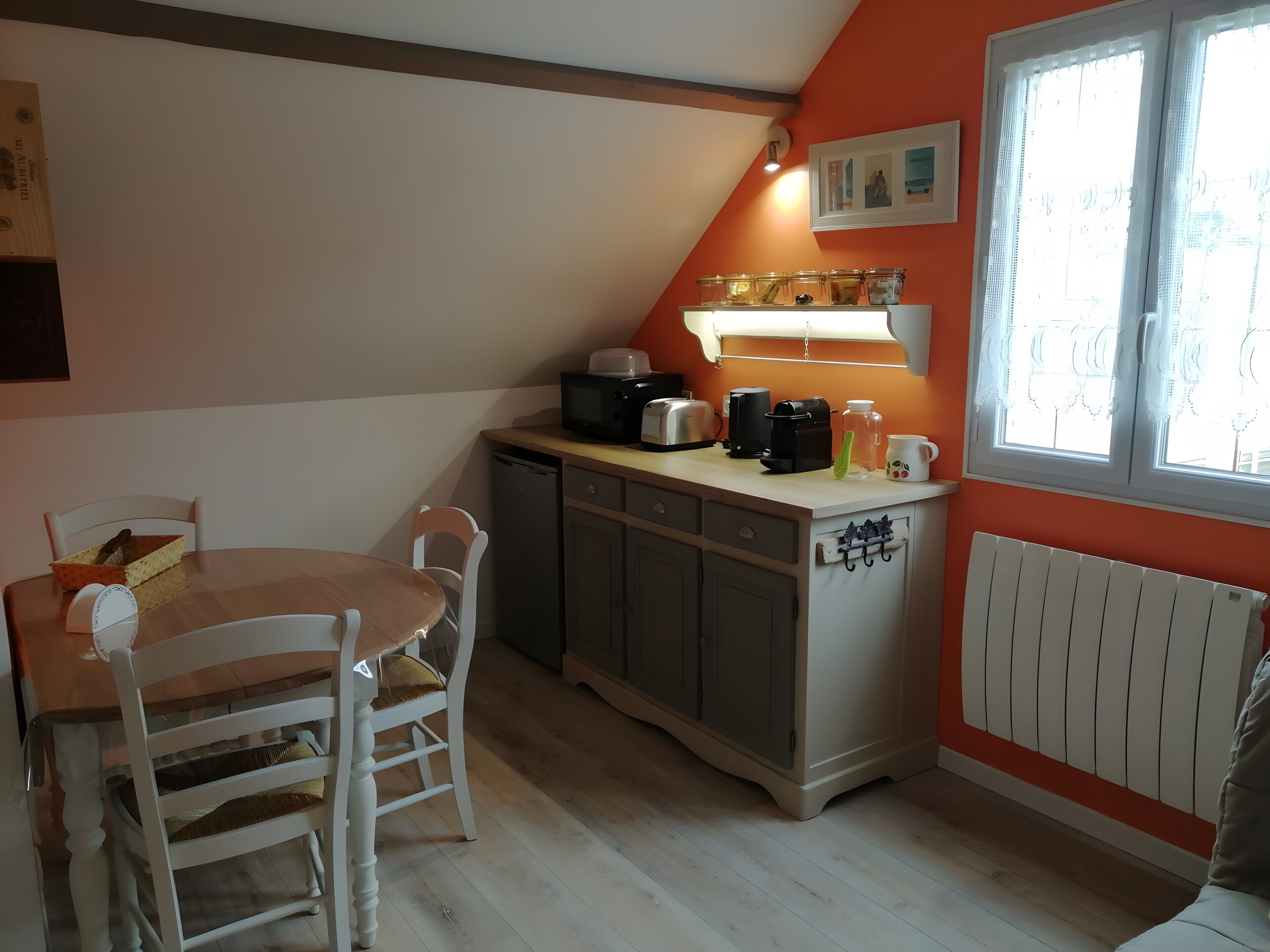 A kitchen with a dining table, chairs, a microwave, toaster, coffee maker, and a window with curtains.
