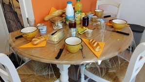 Una mesa redonda de comedor con diversos alimentos y condimentos, rodeada de sillas blancas.