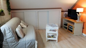 Una sala de estar con un sofá, una mesita con revistas, un televisor sobre un mueble de madera y una estantería de pared.