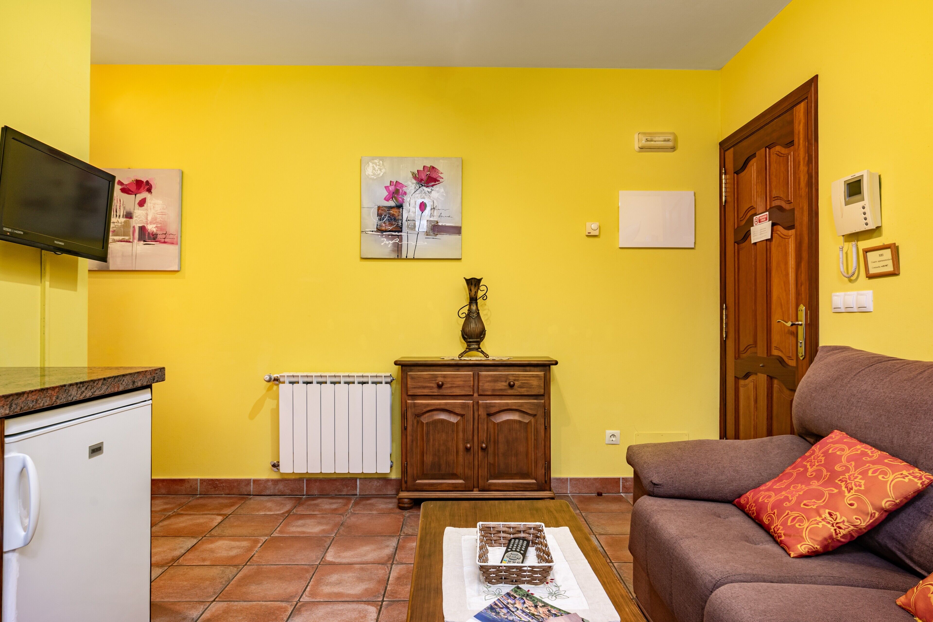 Uma sala de estar com sofá, mesa de centro, armário, televisão e obras de arte nas paredes.