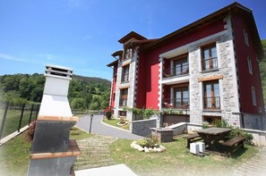 Un immeuble à plusieurs étages, doté d’une façade en pierre, de balcons et d’une allée pavée menant à une table de pique-nique.