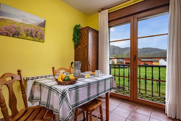 Un coin repas avec une table mise pour le petit-déjeuner, un buffet en bois et une vue sur un paysage verdoyant par une porte vitrée.