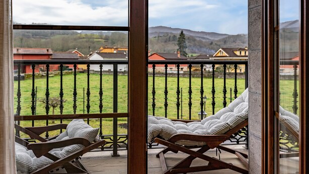 A balcony with a view of a green field and houses, wooden furniture, and a metal railing. - Apartment 'La Viña 3' with Mountain Views and Wi-Fi (Corao)