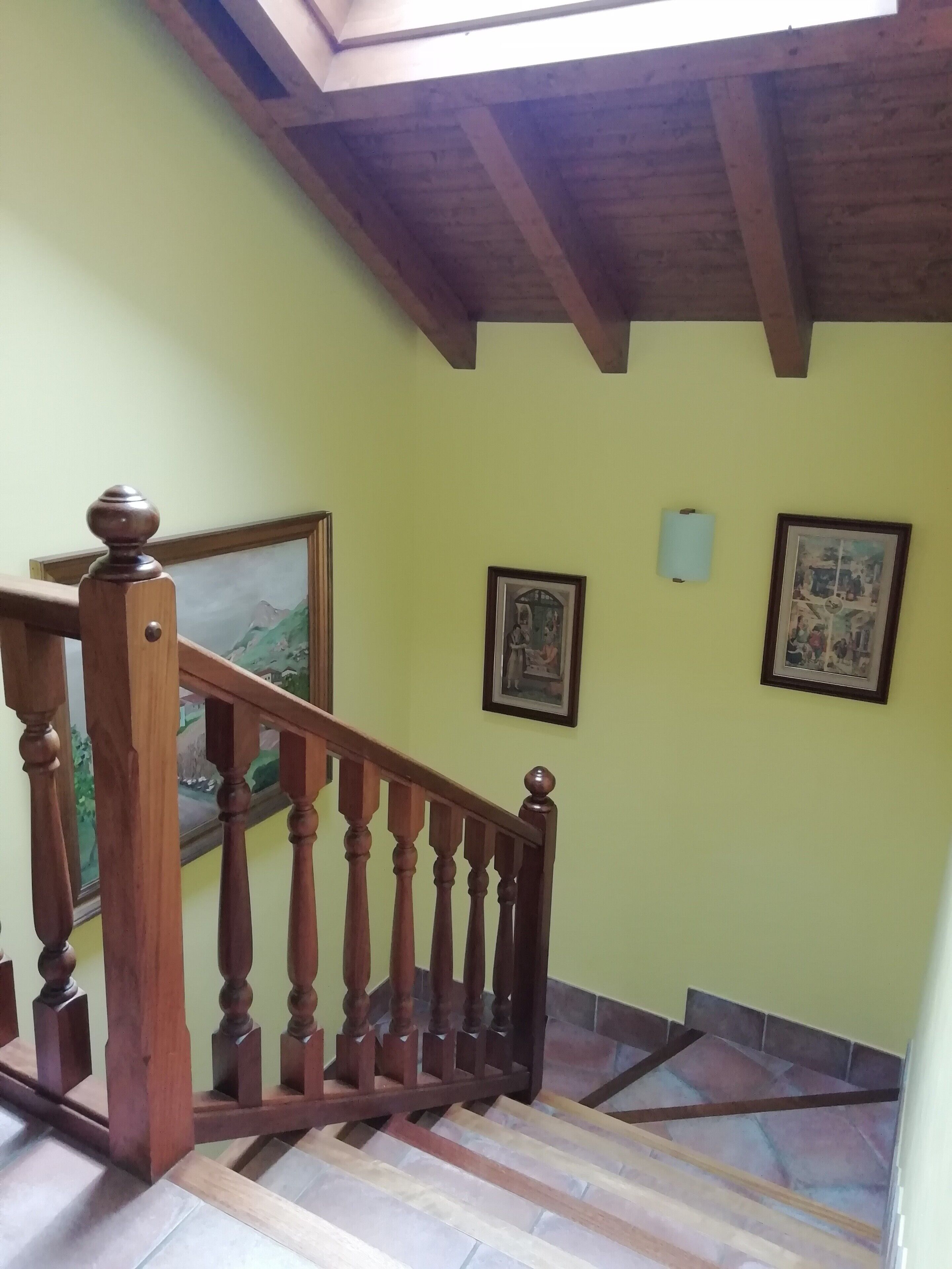 Eine Holztreppe mit Geländer, einem Oberlicht und zwei gerahmten Bildern an der Wand.