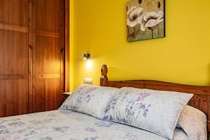 A bedroom with a wooden wardrobe, a bed with floral bedding, a nightstand with a lamp, and a painting on the wall. - Apartment 'La Viña 3' with Mountain Views and Wi-Fi (Corao)