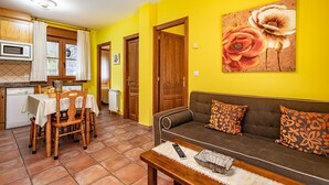 A living room with a sofa, a dining table with chairs, a kitchen area with cabinets and a microwave, and a door leading to another room. - Apartment 'La Viña 3' with Mountain Views and Wi-Fi (Corao)