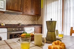 Eine Küche mit Holzausstattung, einer Mikrowelle, einer Kaffeemaschine sowie einem Tisch mit Orangensaft und einem Croissant.